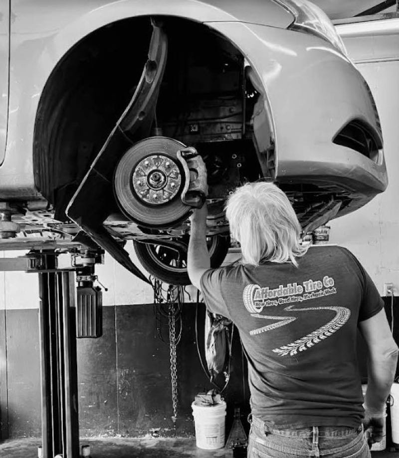 An Affordable Tire Co technician servicing the brakes on a vehicle raised on a lift